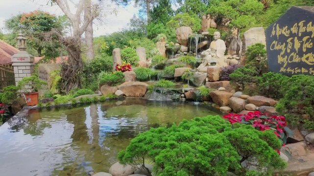 DALAT, VIETNAM, 5 November 2025 &ndash; A serene garden features a statue of a meditating monk beside a cascading waterfall, surrounded by lush greenery and a tranquil pond at Thien Vien Truc Lam