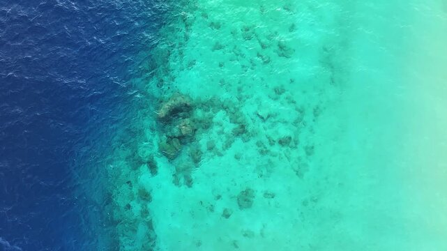 Aerial view of a vibrant coral reef edge meeting deep blue ocean water and shallow turquoise lagoons in Maalhos, Baa Atoll, Maldives.