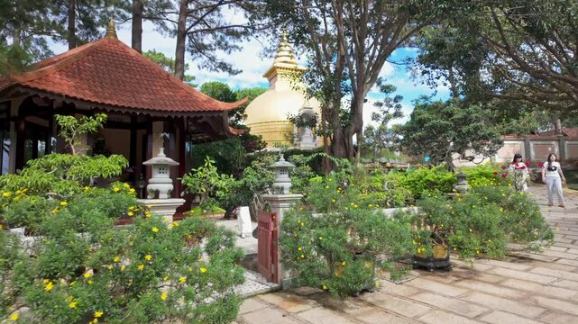 A serene garden with a golden stupa and traditional architecture in Thien Vien Truc Lam, Da Lat, Vietnam. The lush greenery and blooming yellow flowers create a peaceful atmosphere.