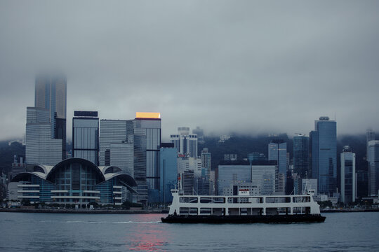 Hong Kong, China - February 01 2025: An HYF passenger ferry crosses Victoria Harbour in front of the iconic Hong Kong Convention and Exhibition Centre (HKCEC) and a fog-covered Wan Chai skyline during