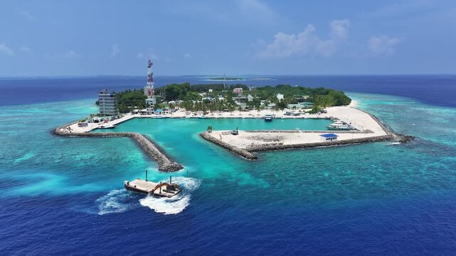 Aerial view of Kamadhoo island featuring a protected harbor, lush tropical vegetation, and vibrant coral reefs surrounded by turquoise waters in Kamadhoo, Baa Atoll, Maldives.