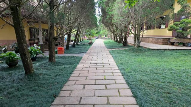 A stone pathway lined with trees and manicured grass leads to a building in a tranquil garden setting. Thien Vien Truc Lam, Da Lat, Vietnam.