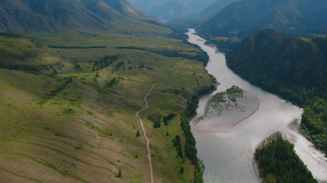 Drone footage of a winding river and sandbar cutting through Ak-Kem Valley, Altai Republic, Russia, with green hills, forested slopes and remote trails
