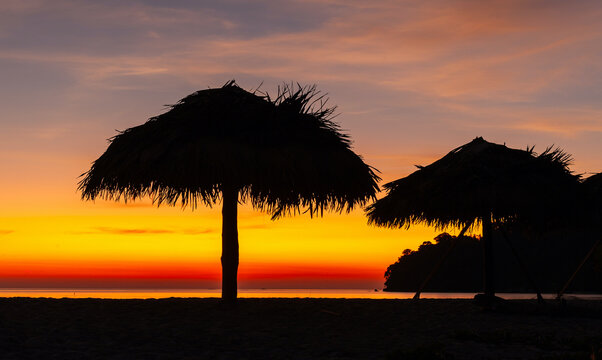 Tropical sunset at Koh Adang, Thailand. Silhouetted beach umbrellas with vibrant sky. Tranquil coastal scene in the Andaman Sea.