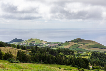 Obraz premium Atlantic Ocean view from San Miguel Island, Azores. Rolling hills and green fields with scattered houses. Moody sky with clouds over the island landscape.