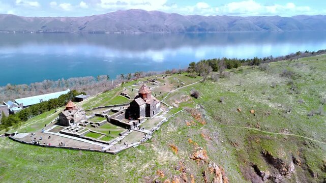 Aerial view of Sevanavank monastery complex on a grassy hill with tourists and the blue waters of Lake Sevan in Sevan, Gegharkunik Province, Armenia.