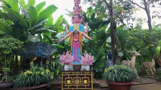 A statue of a multi-armed deity with peacocks and deer adorns a garden in Linh An Pagoda, Da Lat, Vietnam. The statue is a representation of Buddhist or Hindu mythology.