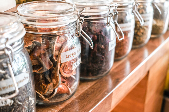 Glass jars, dried herbs, bael fruit, herbal tea, pantry storage, apothecary, spices organized on a rustic wooden shelf in a shop, zero waste, sustainable living concept