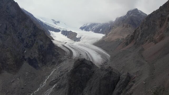 Drone footage of the Aktru Valley with a winding glacier, moraines and steep rocky peaks under cloudy sky, Altai Republic, Russia, remote alpine wilderness