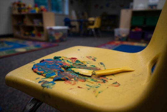 Macro shot of a plastic kindergarten chair with thick opaque modeling clay paste and a snapped tool
