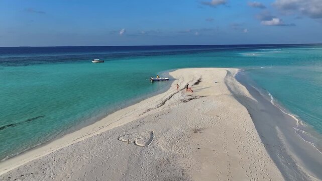 Aerial view of a white sandbank with a heart drawn in the sand, people walking, and a boat anchored in turquoise waters in Goidhoo, Baa Atoll, Maldives.