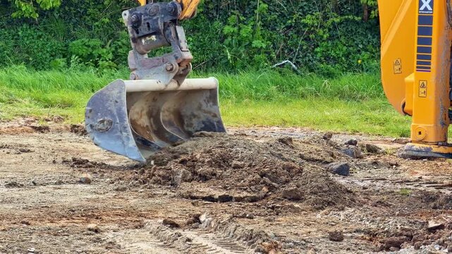 Yellow backhoe loader using its front bucket to move pile of soil on ground