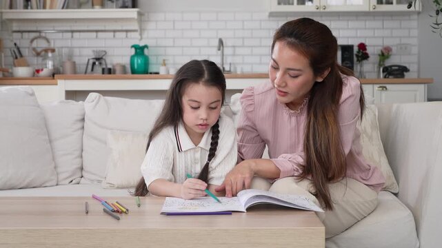 Asian mother looking at cute little daughter drawing with color pencils, Happy family childhood development, creative art education, parenthood childcare, early learning cognitive growth, mother day
