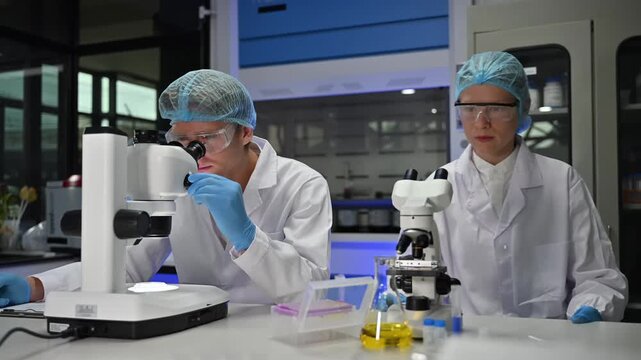 Professional male scientist in protective gear using a microscope for medical research in a laboratory