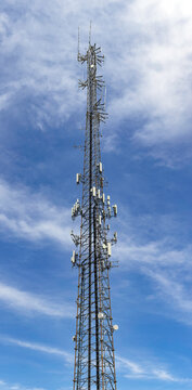 High-resolution vertical panorama of a telecommunications cell tower against a blue sky with clouds, USA