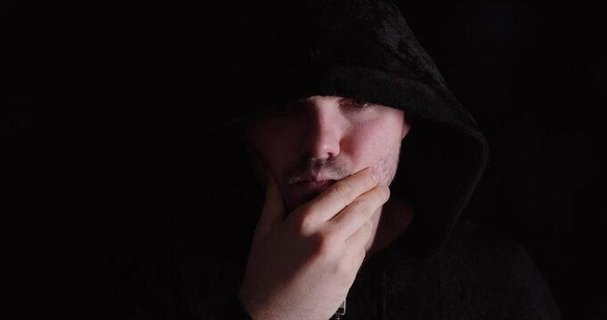 Man in a dark hoodie thinking with hand on chin, symbolizing mystery, contemplation, and inner thoughts.