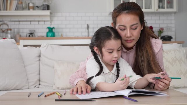 Asian mother looking at cute little daughter drawing with color pencils, Happy family childhood development, creative art education, parenthood childcare, early learning cognitive growth, mother day