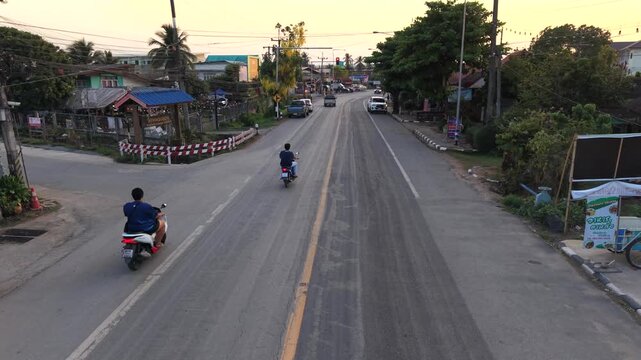 Professional 4K drone view of local traffic and motorcycles on a rural road at sunset, showcasing daily life in a Southeast Asian village.