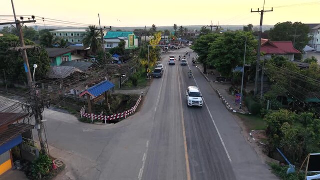 Professional 4K drone view of a rural intersection with local traffic and traditional houses in a Southeast Asian village setting under sunset lighting.