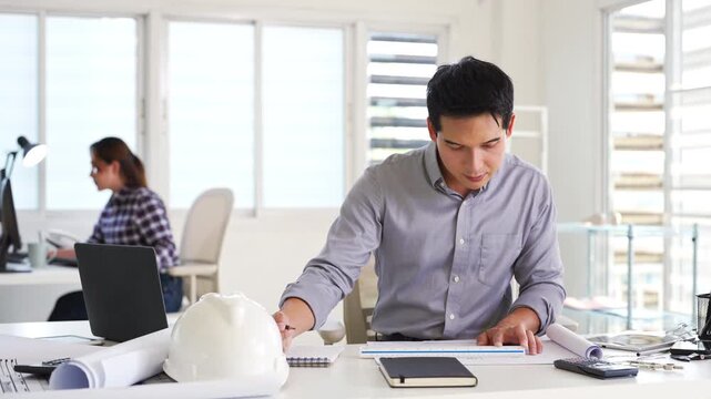 Professional construction engineer checking details on blueprint in construction site office.