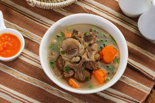Top view of oxtail soup or sop Buntut with vegetables in clean composition, highlighting traditional Indonesian dish and minimal food styling.
