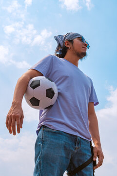 Young Athletic Man Holding Soccer Ball Under Arm Against Blue Sky