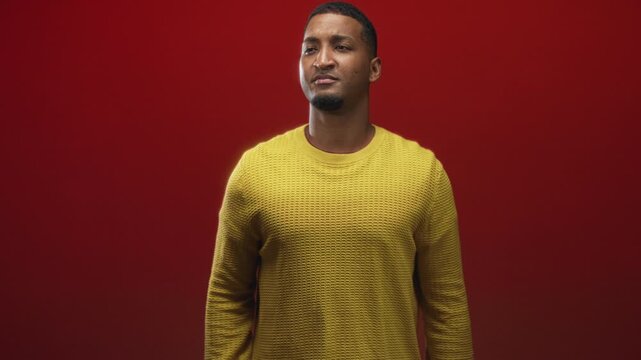 Black man making hashtag hand gesture and later a peace sign with hands, wearing yellow sweater against red seamless backdrop in studio; playful connection confidence.