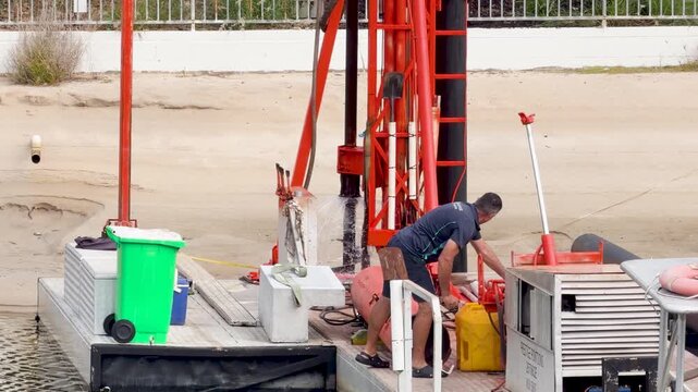 Construction Worker Operating Red Drilling Rig on Waterfront Barge
