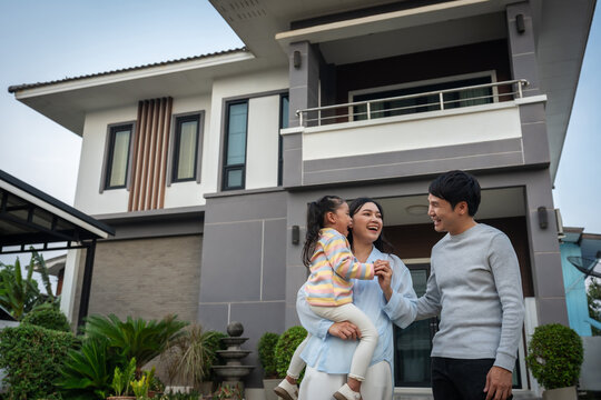 happy family, cheerful father and mother holding and playing with child girl while standing in front of their house