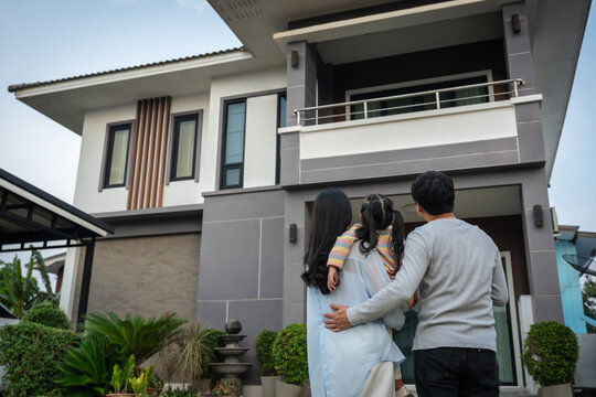 happy family, father and mother holding and hugging with child girl while standing in front of their house