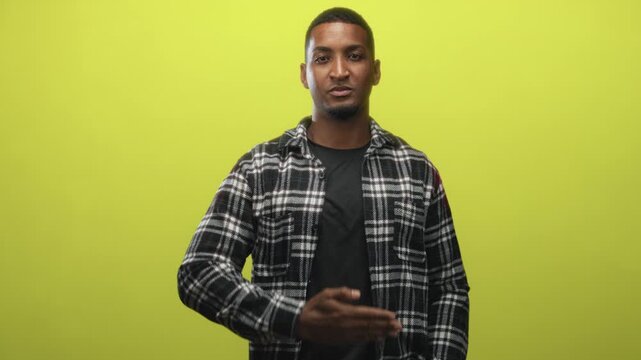 Man covers mouth with hand in studio against lime green backdrop, wearing a plaid flannel shirt and t shirt; playful confidence.