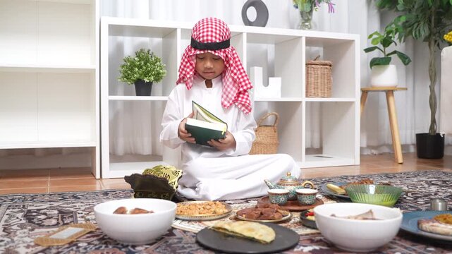 Arab muslim boy hands holding and reading the Holy Quran green book, Wearing traditional white thobe and red keffiyeh, Concept of Islamic religion, faith, Ramadan culture and education