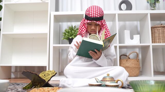 Arab muslim boy hands holding and reading the Holy Quran green book, Wearing traditional white thobe and red keffiyeh, Concept of Islamic religion, faith, Ramadan culture and education