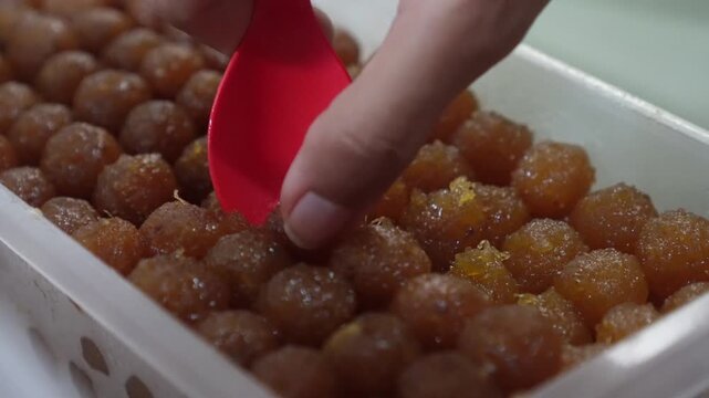 A red spoon scooping glossy, golden pineapple paste spheres.
