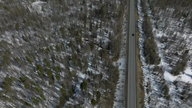 Drone footage of a straight highway cutting through snowy taiga forest in Buryatia, Siberia, Russia, with sparse trees and patches of snow in early spring