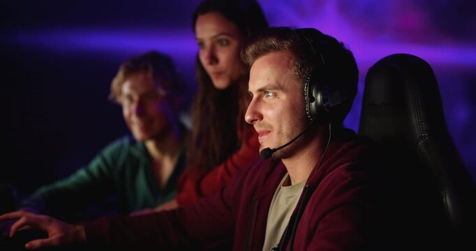 Group of young adult people gamers engaging in online video game play in modern cybercafe. E-sports fun, streaming gaming community, digital entertainment and leisure activity among friends concept