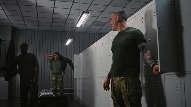 Group of Soldiers in Military Uniforms Gathers in Base Locker Room, Relaxed Conversation, Preparing Equipment, and Adjusting Gear Before Upcoming Mission. Daily Routine and Camaraderie in Army.