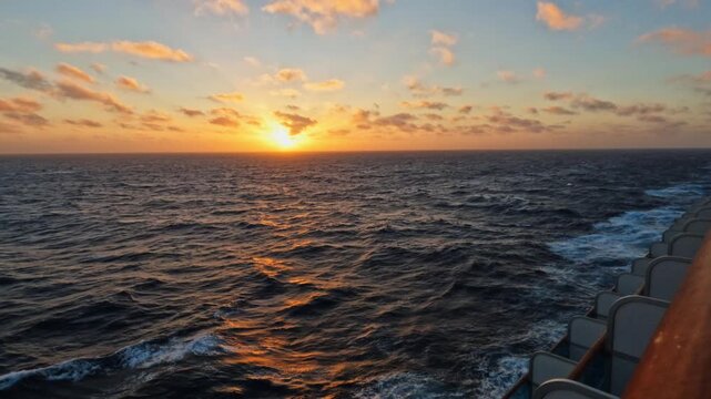 Calm ocean view from a sailing boat at sunset, with golden light reflecting on gentle waves. The horizon glows with warm colors, creating a peaceful and serene atmosphere of travel and freedom