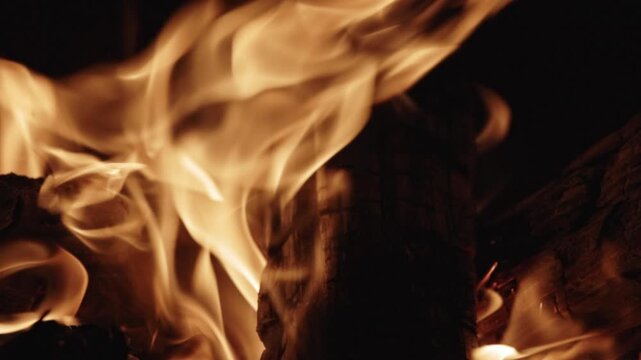 Cinematic slow-motion footage of a flickering fire in a backyard fire pit, featuring detailed close-ups of glowing orange embers and wide shots of dancing flames against a dark evening background.
