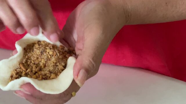 A close-up shot shows hands carefully stretching the edges of a dough wrapper to contain a very generous and overflowing amount of ground peanut filling for a handmade baozi.