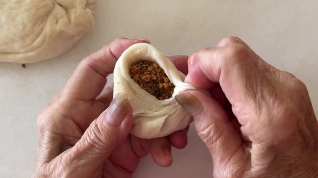 A close-up captures the traditional process of hands skillfully pleating and sealing a handmade baozi filled with a sweet and crunchy ground peanut mixture.