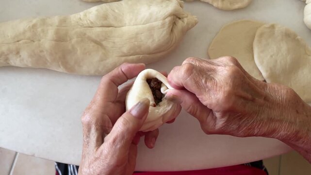 A close-up captures the final steps of hands skillfully pleating and sealing the dough to complete a handmade baozi with minced meat and petai filling.