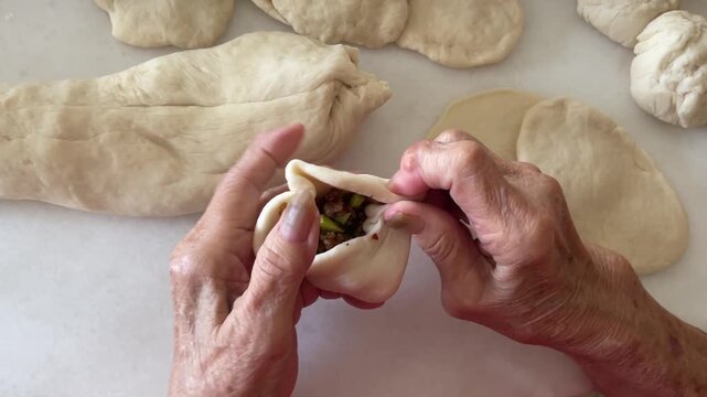 A close-up shot captures hands skillfully pleating and folding the edges of a dough wrapper to seal the savory minced meat and petai filling inside for traditional handmade baozi.