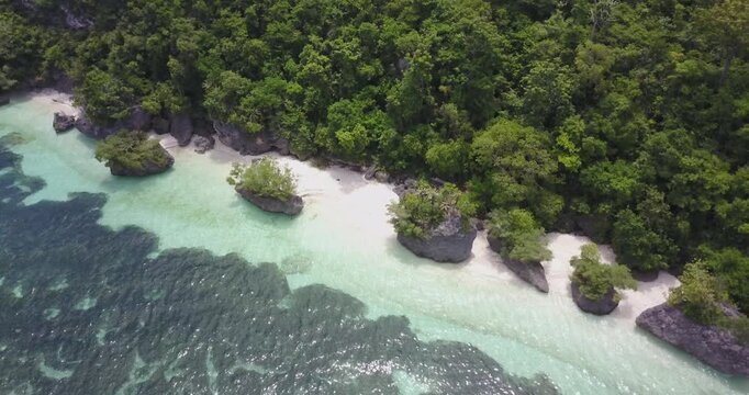 Drone shot flying forward while tilting down towards tropical beach with rocks and jungle coastline, ending facing the shore in Siquijor, Philippines