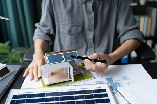 Electrical engineer working on blueprint with solar panel model sustainable energy concept
