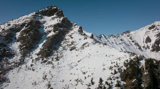 Aerial footage of rugged snow-covered mountain ridge and peaks under clear blue sky near Arshan village, Republic of Buryatia, Russia, winter wilderness landscape
