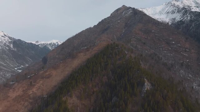 Aerial footage of Love Peak mountain ridge with conifer forest and snowy slopes near Arshan village, Republic of Buryatia, Russia, dramatic wilderness landscape