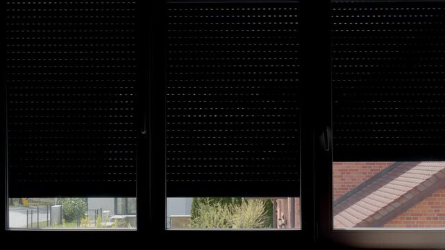 Automatic roller shutters rise on large window letting natural sunlight in room. Blinds open on window. Home automation, smart housing, privacy control, sun protection and window security concepts