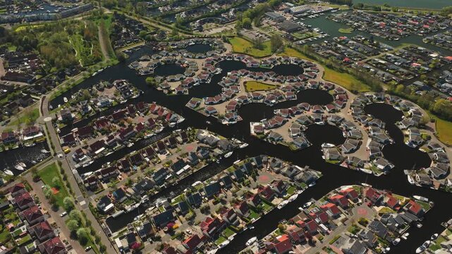 Aerial view of modern residential houses built around circular canals and waterways with docked boats in Lemmer, Friesland, Netherlands.