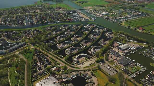 Aerial view of modern circular residential developments and intricate canal systems surrounded by lush green fields and trees in Lemmer, Friesland, Netherlands.